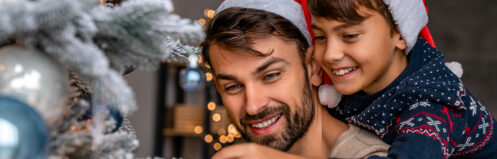 Festive dad and child in Santa hats decorating a Christmas tree