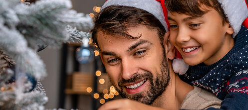 Festive dad and child in Santa hats decorating a Christmas tree