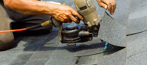 Installer stapling shingles onto a roof